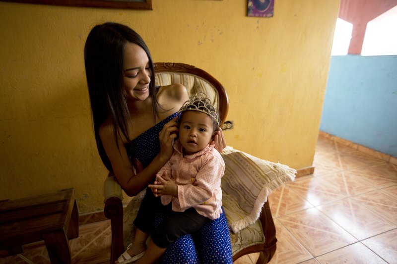 In this July 1, 2018 photo, Johandrys Colls places a crown on her niece Victoria, at her home, at a slum in the outskirts of Caracas, Venezuela. Colls' parents have enrolled her in one of Venezuela's top modeling schools despite their modest income in hopes of transforming their daughter into a sought-after beauty queen. (AP Photo/Fernando Llano)