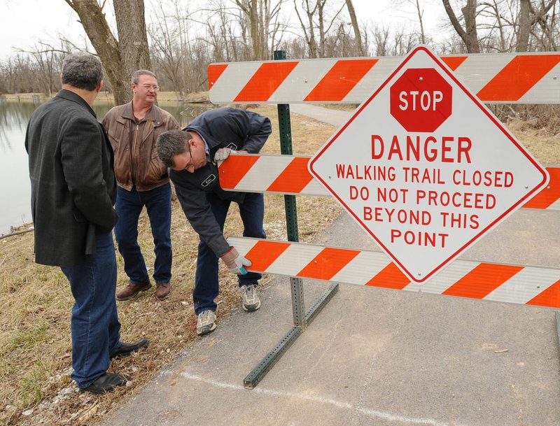 File Photo/NWA Democrat-Gazette/ANDY SHUPE Springdale Mayor Doug Sprouse (left) and Sam Goade, director of Springdale Public Works, watch in March 2010 as Eric Carter installs a sign closing a portion of the walking trail at Lake Springdale along Spring Creek where erosion around the top of the lake's levee in Springdale. Goade is retiring from city after 16 years.