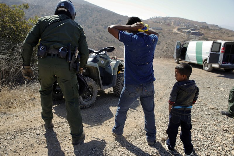 FILE - In this June 28, 2018, file photo, a Guatemalan father and son, who crossed the U.S.-Mexico border illegally, are apprehended by a U.S. Border Patrol agent in San Diego. California will introduce group trials on Monday, July 9, for people charged with entering the country illegally. Federal prosecutors in Arizona, Texas and New Mexico have long embraced these hearings, which critics call assembly-line justice. California was a lone holdout and the Justice Department didn't seriously challenge its position until the arrival of Attorney General Jeff Sessions. (AP Photo/Jae C. Hong, File)
