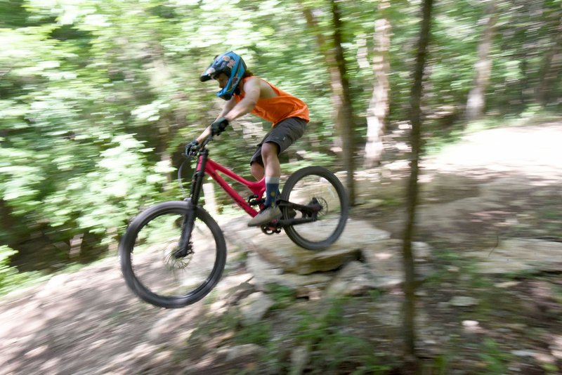 NWA Democrat-Gazette/FLIP PUTTHOFF A rider flies over a rock jump along a downhill trail.