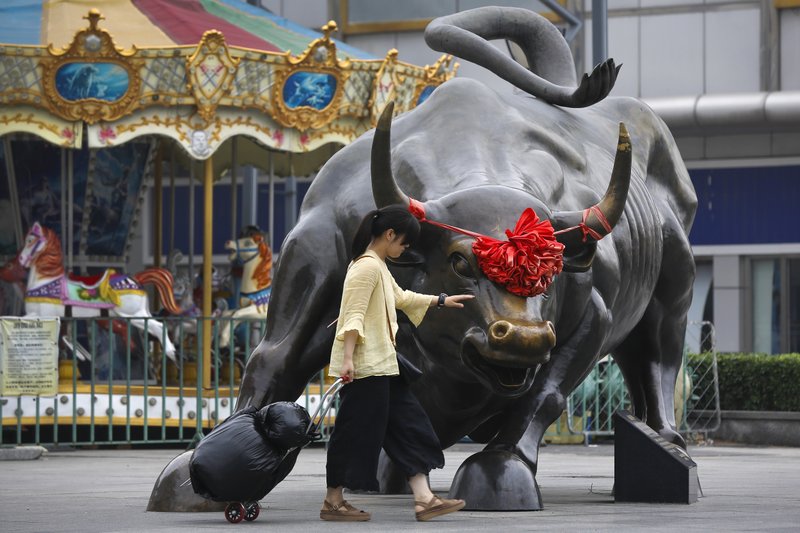 A woman pulls a 2 wheel trolley loaded with goods touches a bull statue on display outside a retail and wholesale clothing mall in Beijing, Monday, July 9, 2018. The trade war that erupted last Friday between the U.S. and China carries a major risk of escalation that could weaken investment, depress spending, unsettle financial markets and slow the global economy. (AP Photo/Andy Wong)