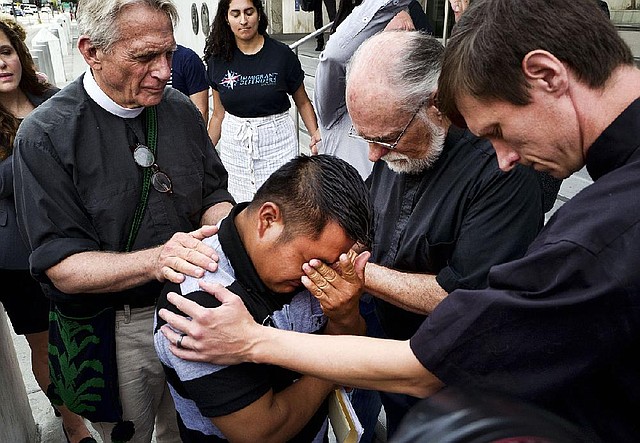 The Revs. Tom Carey (left), David Farley and Matthias Peterson-Brandt (right) pray over Hermelindo Che Coc of Guatemala before a required check-in with immigration officials Tuesday in Los Angeles. Che Coc said he and his 6-year-old son were split up after crossing into Texas in May. He said his son, who was sent to a shelter in New York, feared he was dead.  