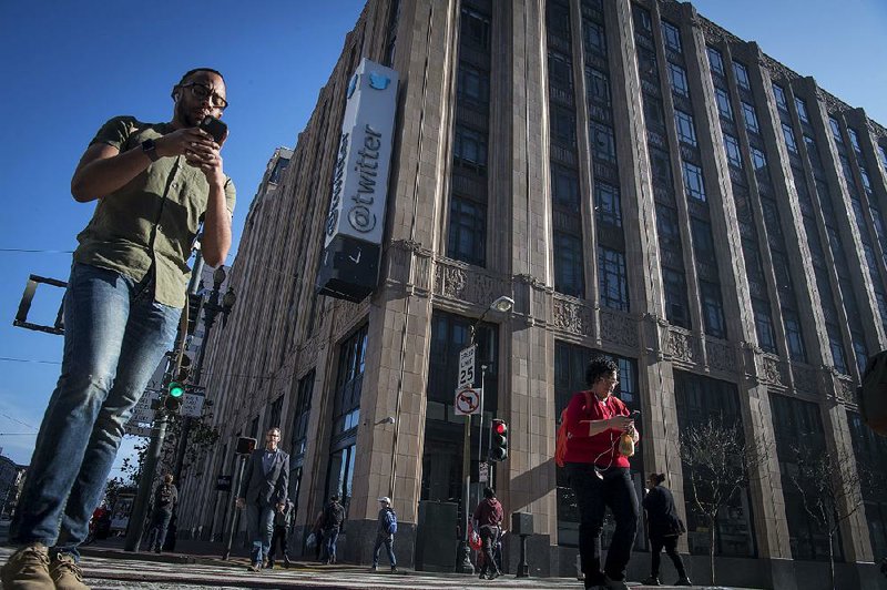 Pedestrians using their mobile phones walk past Twitter headquarters in San Francisco.  
