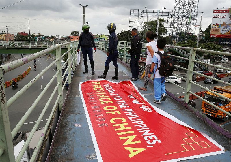 People step around a banner Thursday that’s critical of Philippines President Rodrigo Duterte’s policy toward China and territorial waters. The banner reads “Welcome to the Philippines, Province of China.”  