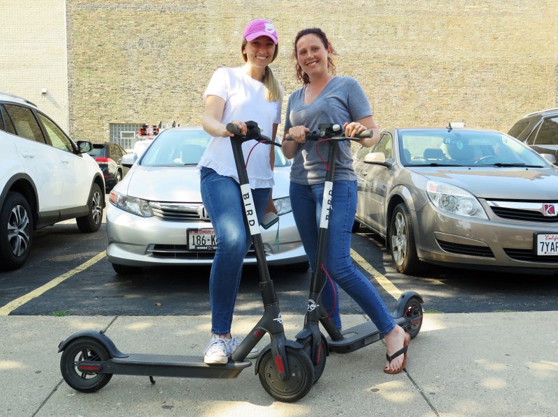 In this Wednesday, July11, 2018 photo, Kirby Bridges, left, and Megan Garlington pose with the Bird scooters they were taking for an afternoon ride in Milwaukee. Milwaukee is suing California-based Bird to stop the company from renting bikes because the city contends they are illegal to operate on streets and sidewalks. (AP Photo/Ivan Moreno)