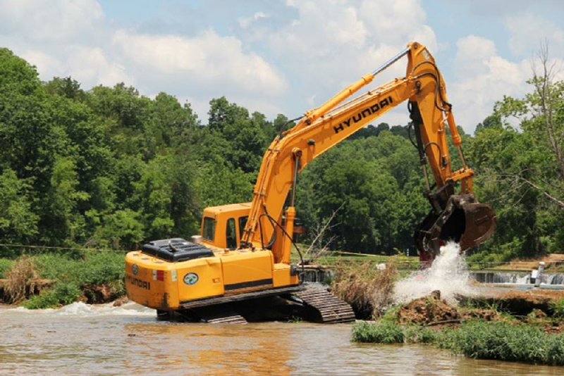 A track hoe works Thursday to fill in a sinkhole in the Spring River that opened last month and claimed the life of a kayaker. The work collapsed the sinkhole roof and filled in the opening, resolving the hazard.  