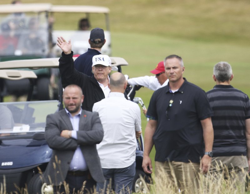 U.S. President Donald Trump waves to protesters while he plays golf at Turnberry golf club, Scotland, Saturday, July 14, 2018. Trump is spending the weekend at his sea-side Trump Turnberry golf resort in Scotland, where aides had said he would be busy preparing for his Monday summit in Helsinki, Finland. (AP Photo/Peter Morrison)