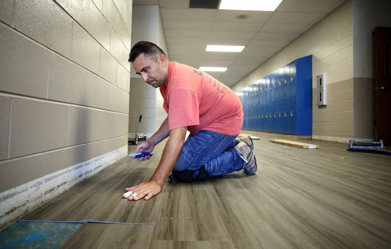 NWA Democrat-Gazette/DAVID GOTTSCHALK Wilfredo Calderon, with Davis Flooring, fits a piece of LVT tile July 6 in the hallway at Woodland Junior High in Fayetteville. New tile is being put down new tile in the hallways and cafeteria of the school. Northwest Arkansas school districts are busy working on facility improvement projects while staff and students are away for the summer break.