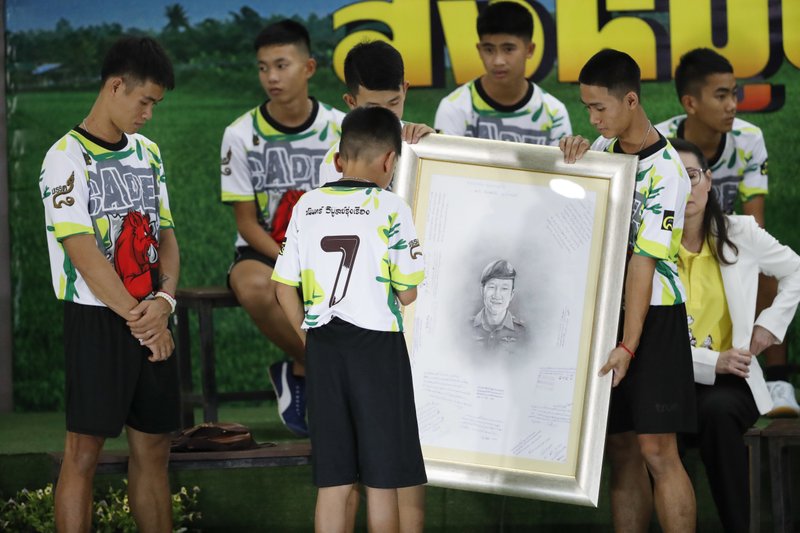 Coach Ekkapol Janthawong, left, and the 12 boys show their respect and thanks as they hold a portrait of Saman Gunan, the retired Thai SEAL diver who died during their rescue attempt, during a press conference in Chiang Rai, northern Thailand, Wednesday, July 18, 2018. The 12 boys and their soccer coach rescued after being trapped in a flooded cave in northern Thailand are recovering well and are eager to eat their favorite comfort foods after their expected discharge from a hospital soon. (AP Photo/Vincent Thian)