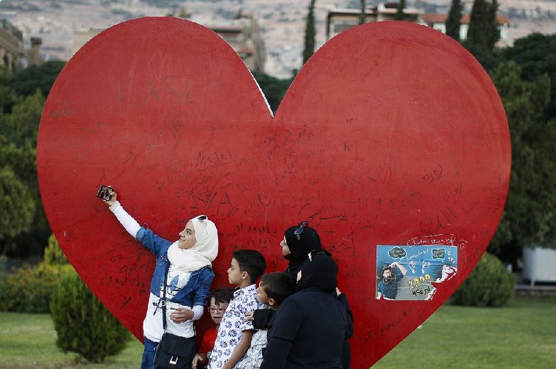 A Syrian girl takes a selfie Wednesday with her family at a Damascus sculpture meant to show love for the war-torn nation’s capital.