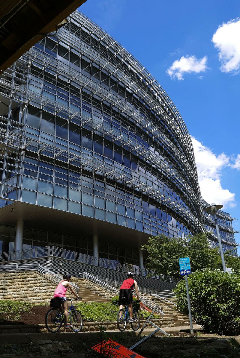 Bicyclists ride past the Alcoa Corp. headquarters building earlier this year on Pittsburgh’s north side. The aluminum producer lowered its 2018 profit projection because of tariffs on material it imports from Canada.  