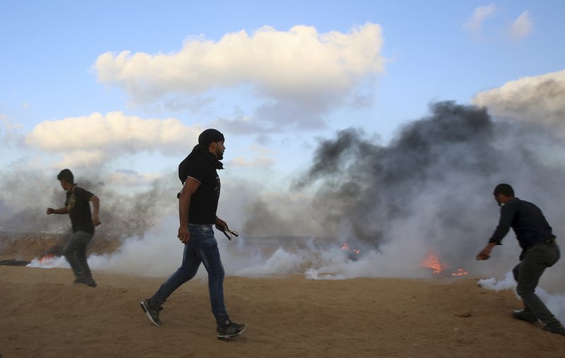 Protesters try to throw back teargas canisters fired by Israeli troops near the fence of the Gaza Strip border with Israel, during a protest east of Khan Younis, southern Gaza Strip, Friday, July 20, 2018. Israel targeted Hamas positions in Gaza, killing four Palestinians on Friday in a series of air strikes after gunmen shot at soldiers near the border, officials said. (AP Photo/Adel Hana)