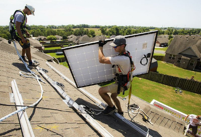 Installer Jarren Stinson carries a solar panel across the roof of a home Friday in Centerton in Northwest Arkansas. The embrace of solar power by a growing number of Arkansas homeowners has set off a debate over reimbursements by utility companies.  