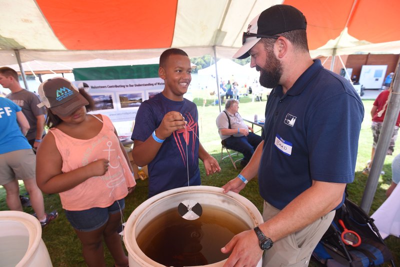 File photo/FLIP PUTTHOFF Taevon Horton lowers a Secchi disk he made into a barrel of muddy water during last year's annual Secchi Day at Prairie Creek park on Beaver Lake as Brad Hufhines with the North American Lakes Management Society explains the tool to measure water clarity. This year's water appreciation festival, which includes food, music and crafts, is scheduled for 9 a.m. to 1 p.m. Aug. 18 at 9300 N. Park Road east of Rogers. Information: Email awilson@bwdh2o.org.