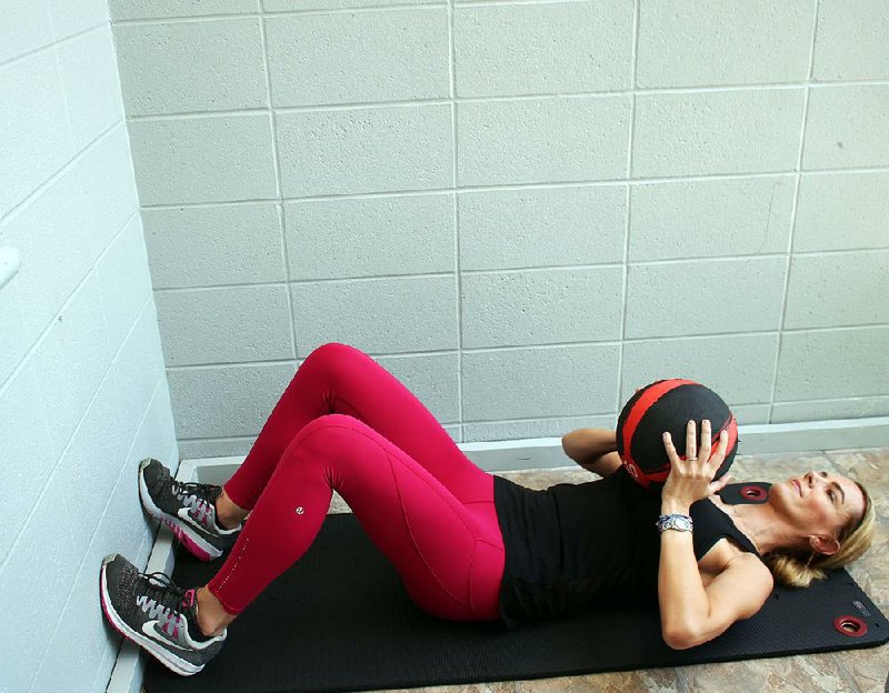 Ashley Bermingham, barre instructor, does steps 1 and 9 of the Med Ball Wall Crawl, a core exercise that is doable pretty much anyplace you can sit facing a wall.