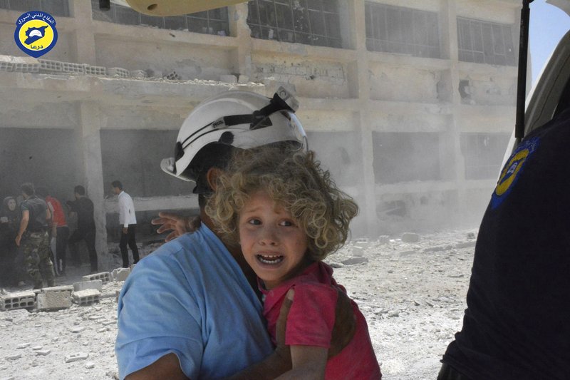 FILE - In this Wednesday, June 14, 2017, file photo, provided by the Syrian Civil Defense group known as the White Helmets, shows a civil defense worker carrying a child after airstrikes hit a school housing a number of displaced people in the western part of the southern Daraa province of Syria. The Israeli military said Sunday it had rescued members of a Syrian volunteer civil organization, known as White Helmets, from the volatile frontier area and evacuated them to a third country, the first such Israeli intervention in Syria's lengthy civil war. (Syrian Civil Defense White Helmets via AP, File)