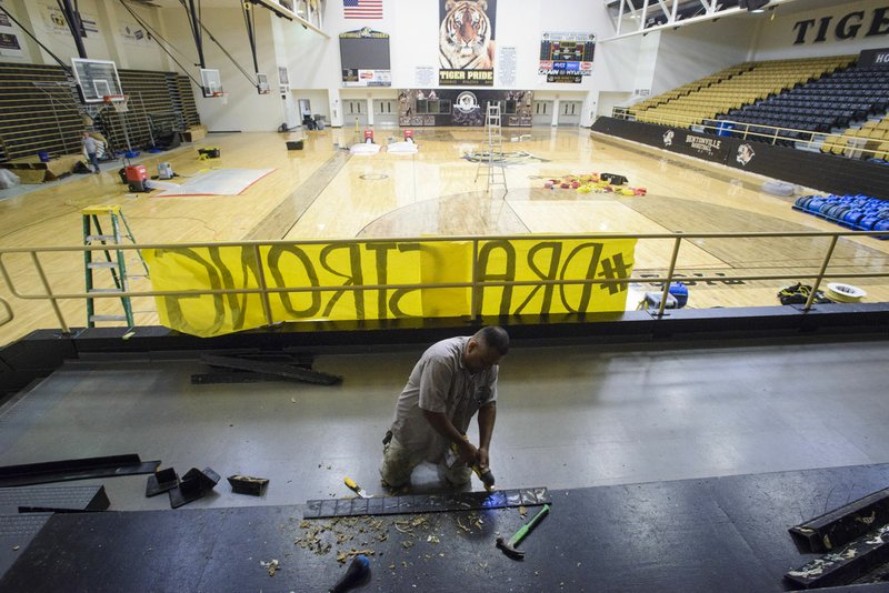 NWA Democrat-Gazette/CHARLIE KAIJO Jose Portillo, a contractor from NWA Restore It, removes old glue from base moldings Monday at Bentonville High School's gymnasium. The moldings had to be removed to dry water underneath the basketball court after rain from a storm about two weeks ago leaked through the roof of the gym causing three to four inches of water to flood the floor, said Peter Hader from NWA Restore It.
