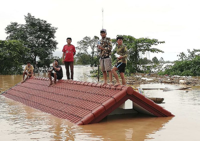 Laotian villagers surrounded by flooding from a collapsed hydroelectric dam take refuge on a rooftop Tuesday in southeastern Attapeu province. The South Korean-constructed dam collapsed Monday evening, flooding villages and sweeping away houses. Several people were known dead, but hundreds were missing and more than 6,600 were left homeless.  