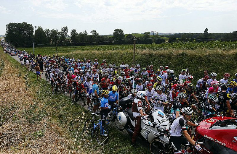 Riders wait on the road after Tuesday’s 16th stage of the Tour de France was interrupted after protesting farmers blocked the road with hay bales about 18.5 miles into the 135.5-mile stage. 