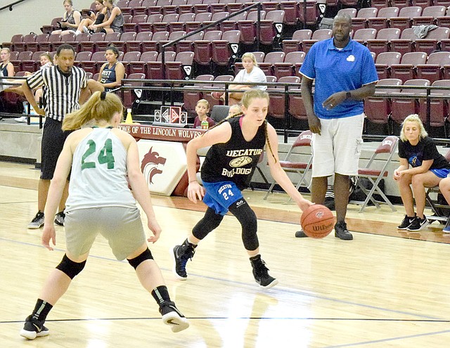 Westside Eagle Observer/MIKE ECKELS With new Lady Bulldogs coach Fess Thompson (standing, right) watching, Decatur's Sammie Skaggs (24, center) moves the ball around a Lady Pirate defender during the Decatur-Greenland JV scrimmage contest in the new gym at Lincoln High School July 19.