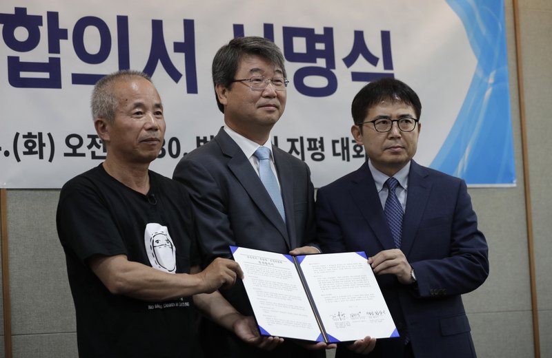 Hwang Sang-gi, left, father of former Samsung semiconductor factory worker Hwang Yu-mi who died from leukemia in 2007, Kim Ji-hyung, center, a chairman of the Mediation Committee and Kim Sunsig, right, senior vice president of Samsung Electronics, right, pose for the media during a signing ceremony in Seoul, South Korea, Tuesday, July 24, 2018. Samsung Electronics and a group representing ailing Samsung computer chip and display factory workers say they have agreed to end a years-long standoff over compensation for deaths and grave illnesses among Samsung workers. (AP Photo/Lee Jin-man)