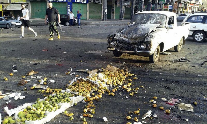 Two men walk past the site of a suicide attack Wednesday in Sweida, Syria. The bombing in southern Syria was part of a coordinated wave of violence by the Islamic State that left scores of people dead.  