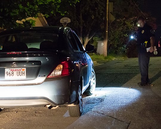 The Sentinel-Record/Rebekah Hedges CRIME SCENE: Hot Springs police Officer 1st Class Brian Branstetter shines his flashlight on broken glass near a car at the scene where two women were shot Thursday night in the 200 block of Rector Street.