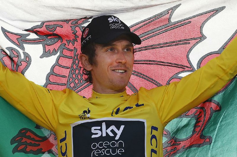 Britain's Geraint Thomas, wearing the overall leader's yellow jersey, holds the Welsh flag on the podium after the twenty-first stage of the Tour de France cycling race over 116 kilometers (72.1 miles) with start in Houilles and finish on Champs-Elysees avenue in Paris, France, Sunday July 29, 2018.