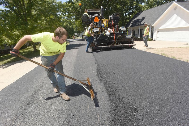 NWA Democrat-Gazette/FLIP PUTTHOFF Corbin Elders (left) with Benton County's Road Department works Wednesday with a crew paving Ravenshoe Road near Beaver Lake. The county revised its 2017 road plan and developed its 2018 plan and the 2019 road plan based on the information from an assessment.
