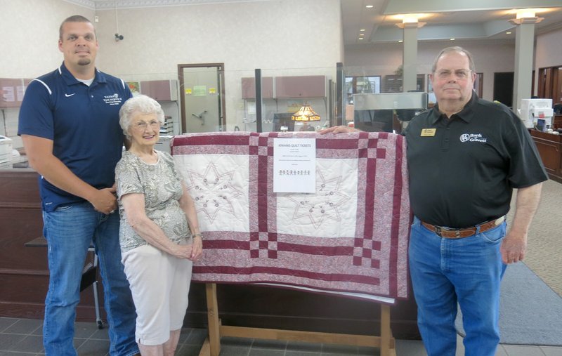 Westside Eagle Observer/SUSAN HOLLAND Betty Howard poses with Kiwanis Club members Josh Stone and Rickie Stark and the quilt she made and donated to their club. The quilt, which features blocks with embroidered stars and flowers, will be raffled at the Kiwanis pancake breakfast on Gravette Day. It is on display at Bank of Gravett and later will be displayed at Arvest Bank. Tickets can be purchased at either bank or from any Kiwanis member. All proceeds go toward Kiwanis service projects.
