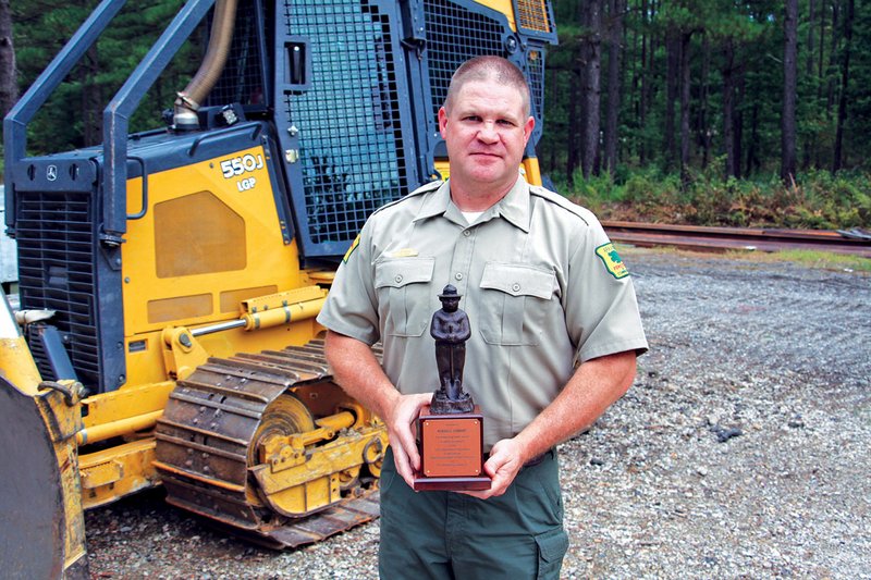 Russell Cowart, a ranger for the Garland County Forestry Commission, stands in front of one of the bulldozers the commission uses to help fight and prevent wildfires. Cowart was recently awarded the Bronze Smokey Bear Award, the highest honor awarded by the U.S. Forest Service for outstanding work and program impact in wildfire prevention.