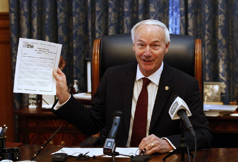 Gov. Asa Hutchinson displays a 2013 release documenting a previous record for a low Medicaid growth rate during a news conference Friday at which he touted his administration’s efforts to control the growth of Medicaid. 
