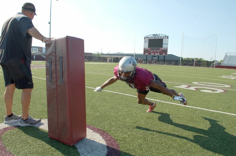 Graham Thomas/Siloam Sunday Siloam Springs head coach Brandon Craig holds a tackling dummy as senior cornerback Primo Agbehi dives in for a tackling drill at football practice Thursday at Panther Stadium.