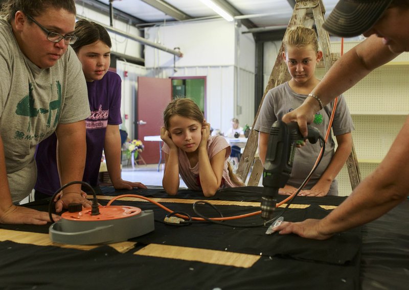 NWA Democrat-Gazette/CHARLIE KAIJO Shannon Brown of Maysville (right) drills as Tonya Farrister (from left), Kelli McGarrah, 10, Kinzie McGarrah, 7, and Laney Brown, 13, from the Maysville 4-H Club watch Saturday at the Benton County Fairgrounds in Bentonville. Vendors prepared their booths ahead of the Benton County Fair which is set to begin Tuesday.