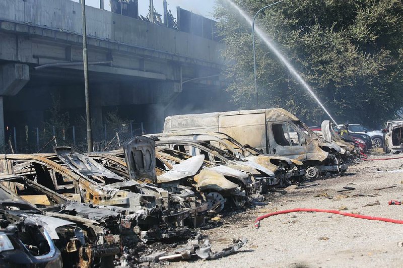 A firefighter sprays down charred vehicles under the highway on the outskirt of Bologna, Italy, on Monday, after a tanker truck carrying flammable material exploded, killing at least two peo- ple and injuring up to 70 as it partially collapsed the overpass, police said. 