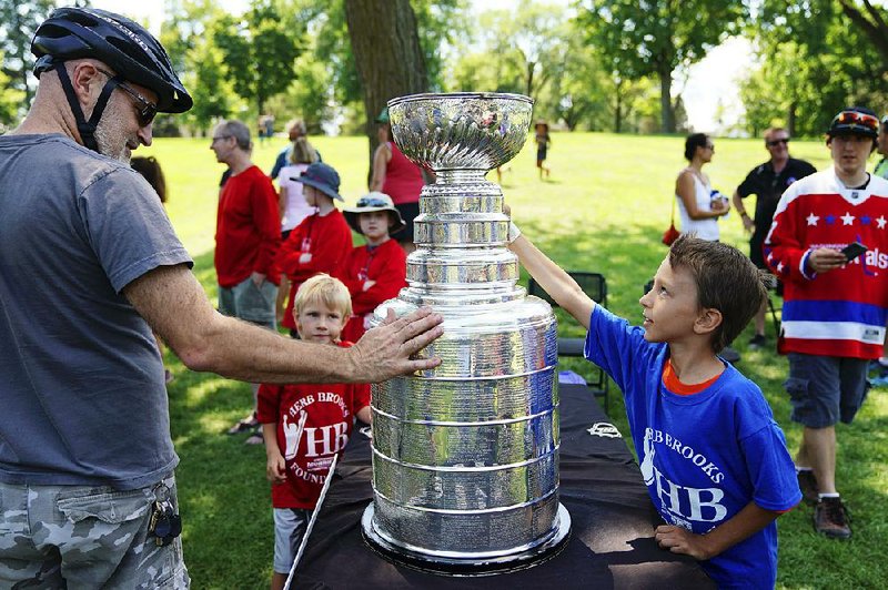 Mark Bouchard (left) and Will Grams touch the Stanley Cup on July 21 at Powderhorn Park in Minneapolis. In its travels around the globe, caviar to ice cream has been used to fill the bowl of the trophy.  