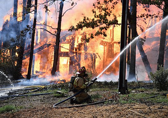 The Sentinel-Record/Grace Brown INFERNO: A volunteer firefighter works to prevent a fully involved structure fire from spreading to nearby homes at 654 Springwood Road on Monday.