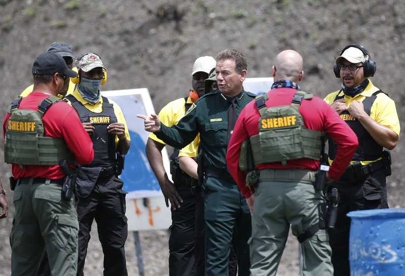 In this Monday, July 30, 2018 photo, Broward County Sheriff Scott Israel, center, talks with trainers and Broward County Public Schools newly-hired armed guardians during firearms training at BSO's gun range at Markham Park in Sunrise, Fla.  (AP Photo/Wilfredo Lee)