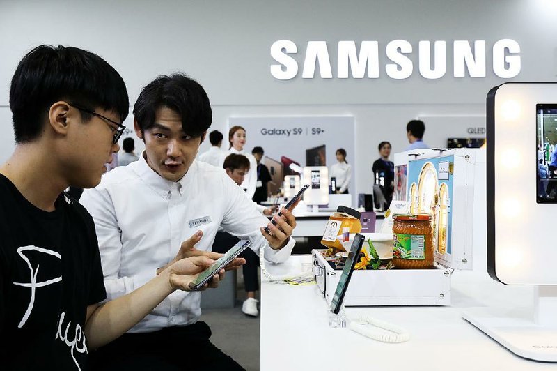 A booth attendant (right) demonstrates a Samsung Electronics Co. smartphone to a visitor in May at the World IT Show 2018 in Seoul, South Korea. The company plans to invest in new products such as artificial intelligence and 5G. 