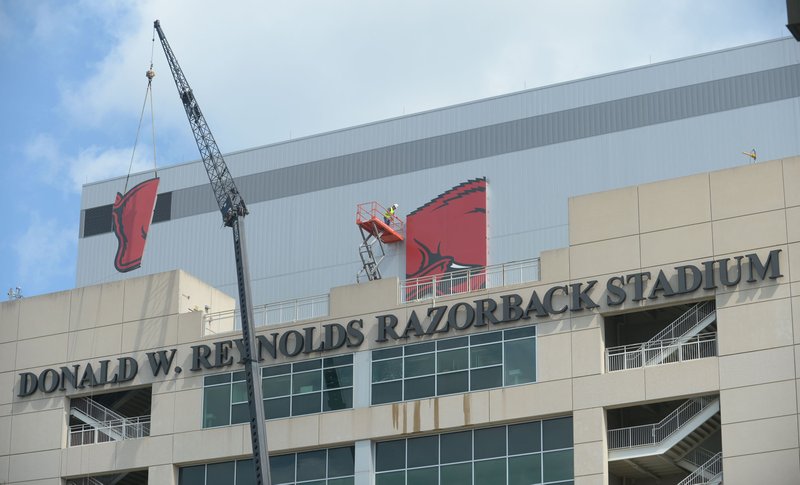 Workers with Multi-Craft Contractors and Sign Studio work to guide a panel of a large Razorback mascot logo Thursday, Aug. 9, 2018, onto the south side of Razorback Stadium in Fayetteville. The sign is being attached to the large video screen as a part of a renovation to the stadium.
