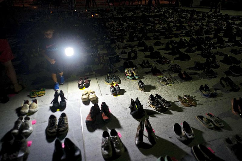 A child shines a light June 1 on hundreds of shoes at a memorial in front of the Puerto Rico Capitol in San Juan for people who died as a result of Hurricane Maria.