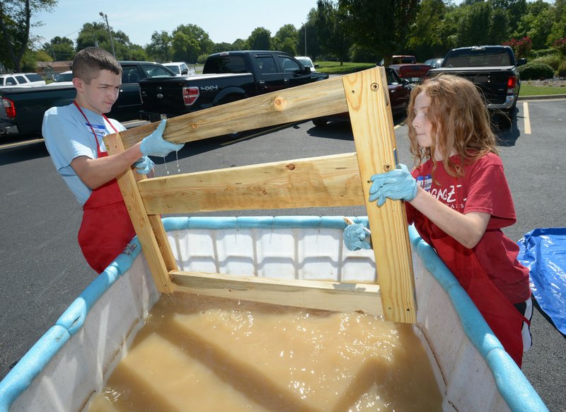 NWA Democrat-Gazette/ANDY SHUPE Volunteers Dalton Maloch (left) and Addison Sexton wash finished bed frames Aug. 4 at First Baptist Church in Rogers. Nearly 70 volunteers built 39 beds in three hours to be delivered to children in need through the new local chapter of Sleep in Heavenly Peace.