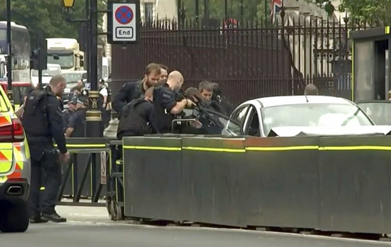 In this frame grab taken Tuesday, Aug. 14, 2018 armed police train their weapons on a car crashed into security barriers outside the Houses of Parliament stands to the right of a bus in London. London police say that a car has crashed into barriers outside the Houses of Parliament and that there are a number of injured. (ITN via AP)