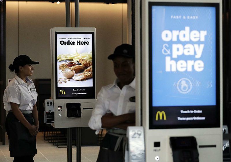 Employees stand near new self-order kiosks last week in the McDonald’s Corp. flagship restaurant in Chicago. The burger chain and its franchisees are modernizing their restaurants nationwide. 