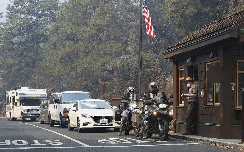 Park Ranger Alex Martinez wears a mask Tuesday as he passes out maps and directions to visitors at the California Highway 140 gate as Yosemite National Park reopens after being closed because of wildfires. 