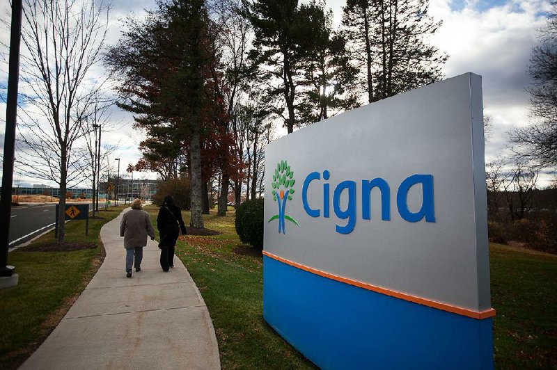 People walk near the Cigna Corp. headquarters building in Bloomfield, Conn. Investor Carl Icahn has relented and says he won’t seek to block the company’s acquisition of Express Scripts. 