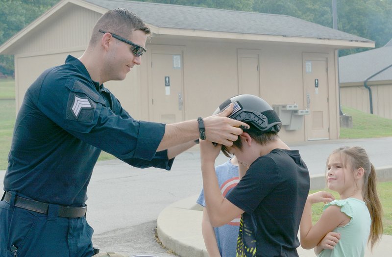 Keith Bryant/The Weekly Vista Sgt. Ross Conn (left) helps Bella Vista resident Josiah Everett, 12, try on one of the tactical response team's helmets, which are size-adjustable and feature attachment points for a wide array of equipment. Macie Everett, 7, watches.
