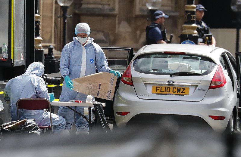 Forensics officers work near the car that crashed into security barriers outside the Houses of Parliament in London, Tuesday, Aug. 14, 2018. Authorities said in a statement Tuesday that a man in his 20s was arrested on suspicion of terrorist offenses after a silver Ford Fiesta collided with a number of cyclists and pedestrians before crashing into the barriers during the morning rush hour. (AP Photo/Frank Augstein)