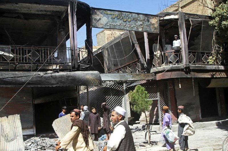 People stand in front of burned-out shops Wednesday after a Taliban attack in Ghazni, Afghanistan.  