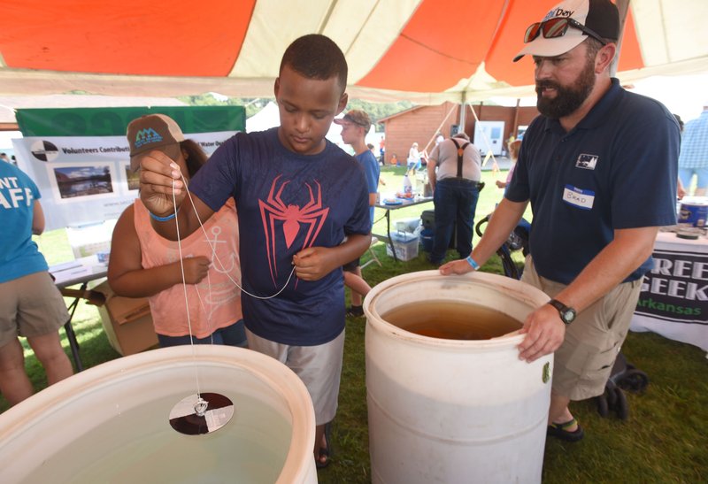 NWA Democrat-Gazette/FLIP PUTTHOFF
Taevon Horton, 13, lowers a Secchi Disk he made into a barrel of water Saturday Aug. 19 2017 during the annual Secchi Day at Prairie Creek park on Beaver Lake, Brad Hufhines (right), with the North American Lakes Management Society, explains how a Secchi Disk is used to measure water clarity. Secchi Day, a water quality awareness event, featured games and exhibits about water issues. 